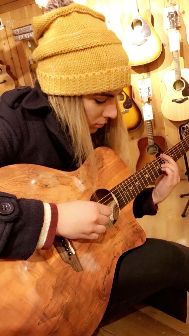 Adrianne playing an acoustic guitar in a music shop